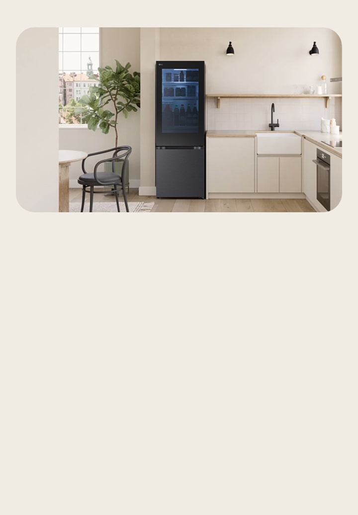 LG tall fridge freezer with a glass front in a beige and wood-toned kitchen. The transparent door reveals green-lit shelves with neatly organised groceries. A table and plant are nearby.