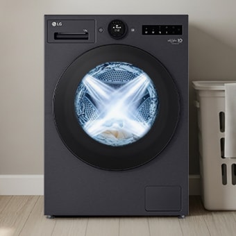 LG Black front loading washer in a modern multipurpose room. A laundry basket sits next to the machine, and the interior of the dryer is illuminated.	