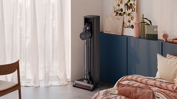 LG All-in-One Tower in black upright beside blue cabinet, sheer white curtains, and a bed with pink quilt.