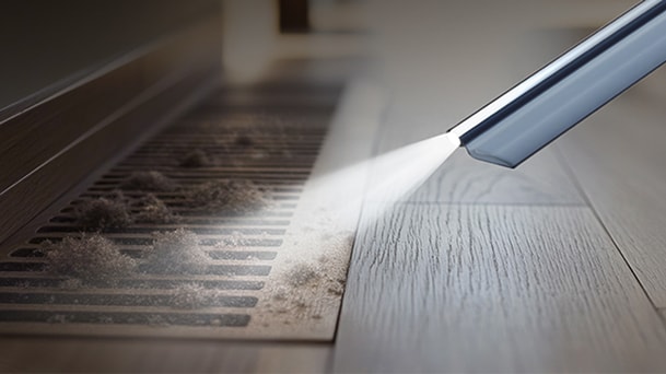 LG vacuum cleaner crevice nozzle targets dust along a vent grate edge on a wooden floor.