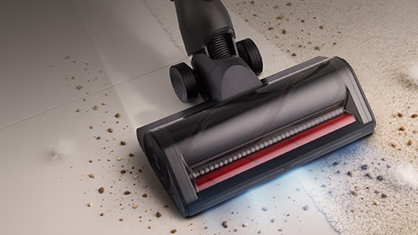 LG black vacuum cleaner powered floor head shows a red brush roller and blue light while it cleans debris near the carpet.