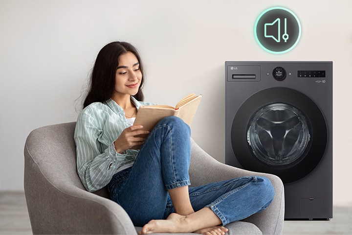 The woman is sitting at a table reading a book and showing icons and washing machines that have less noise next to her