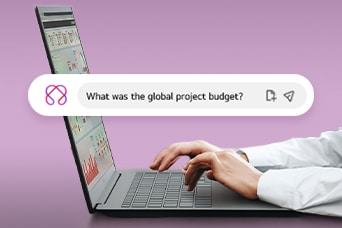 This image shows hands typing on a laptop with a search bar displaying the question, 'What was the global project budget?'
