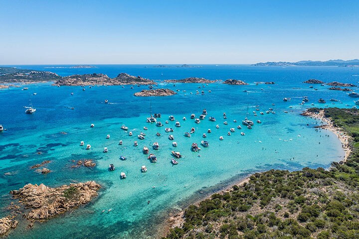 Overhead shot of boats on the clear waters off Sardinia's coast, ideal for experiencing with camping gadgets.