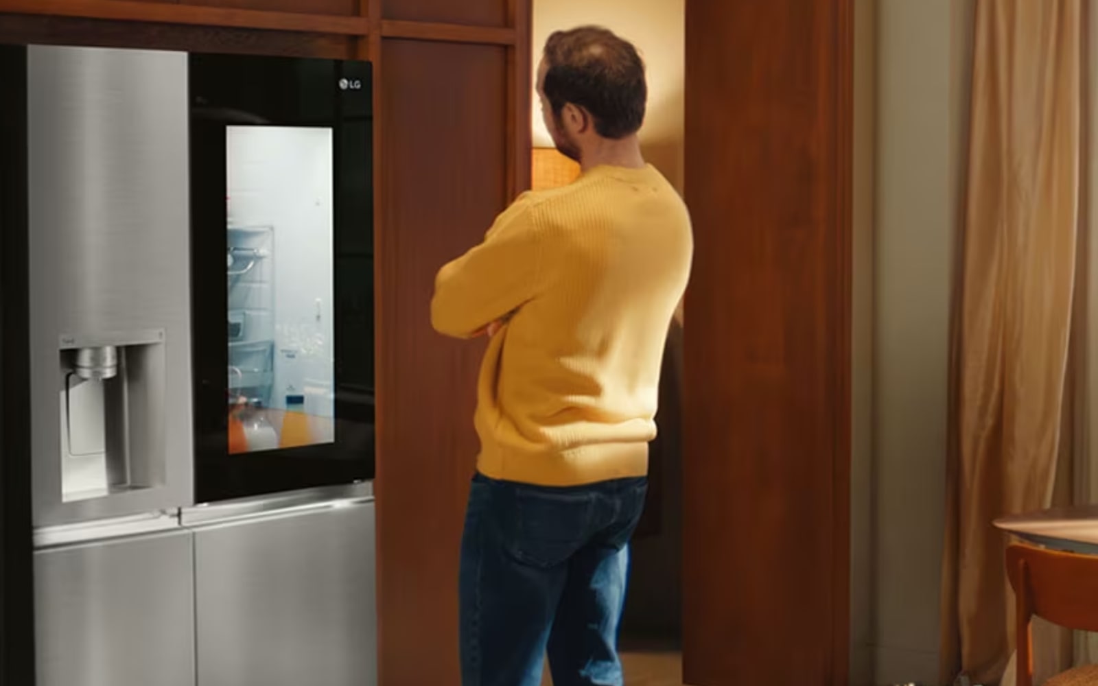 A man in a yellow jumper admires an LG fridge with an illuminated InstaView™ panel, allowing him to see inside.