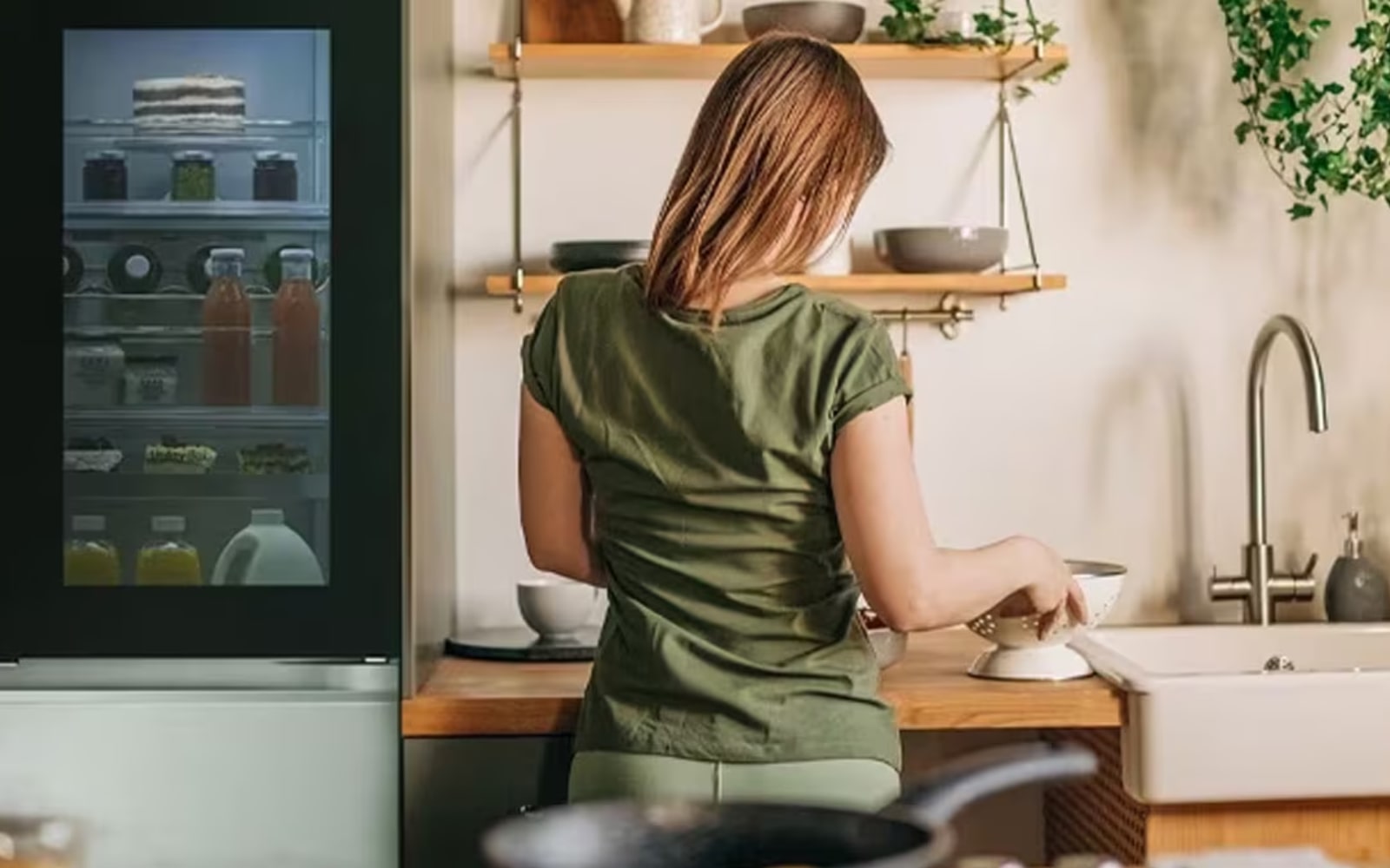 A person is standing in the kitchen organising items on the kitchen counter. There’s an LG fridge next to them with an illuminated InstaView™ panel, filled with juices and pastries.