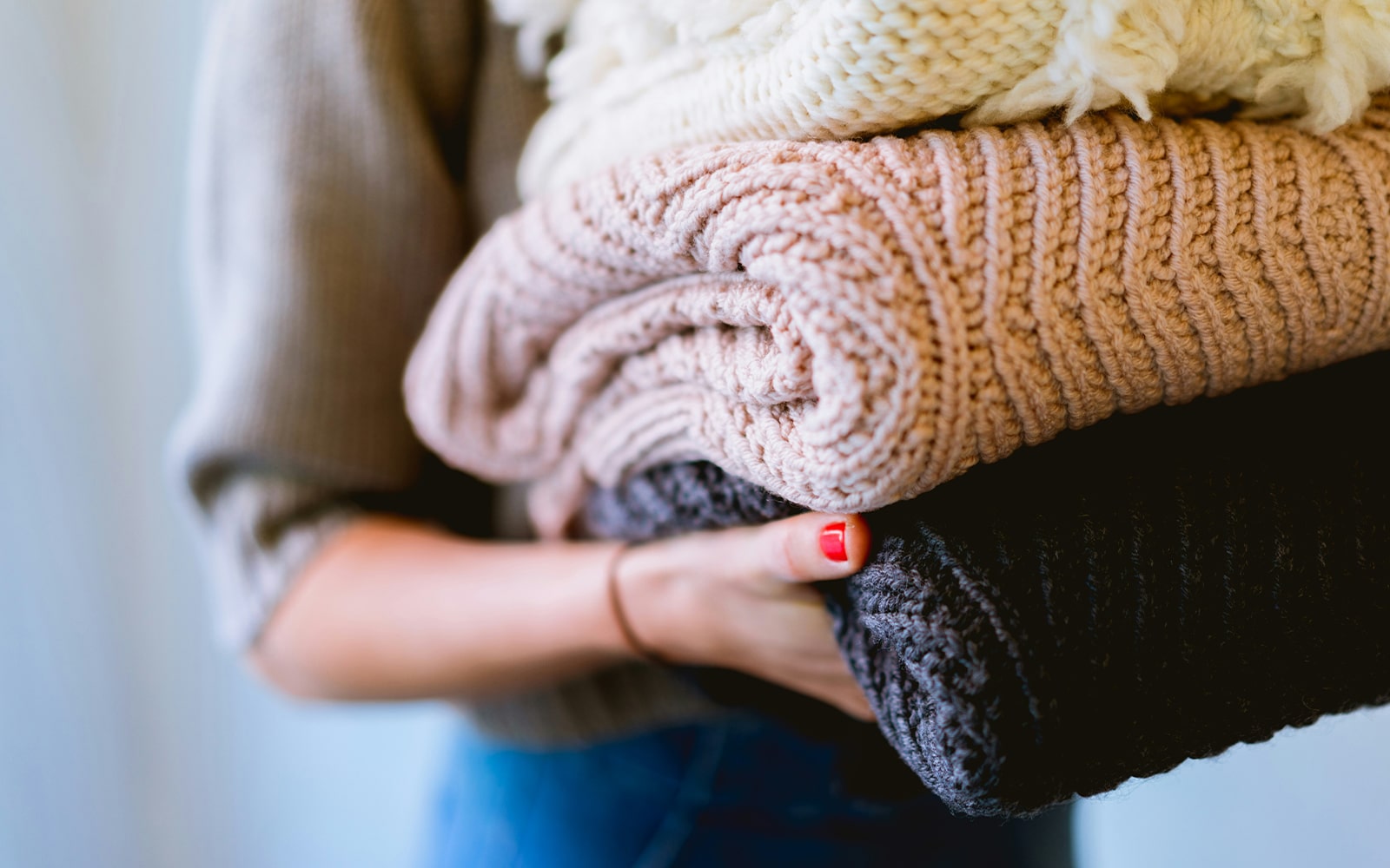 Person holding a stack of folded sweaters in various shades including cream, pink, and black.