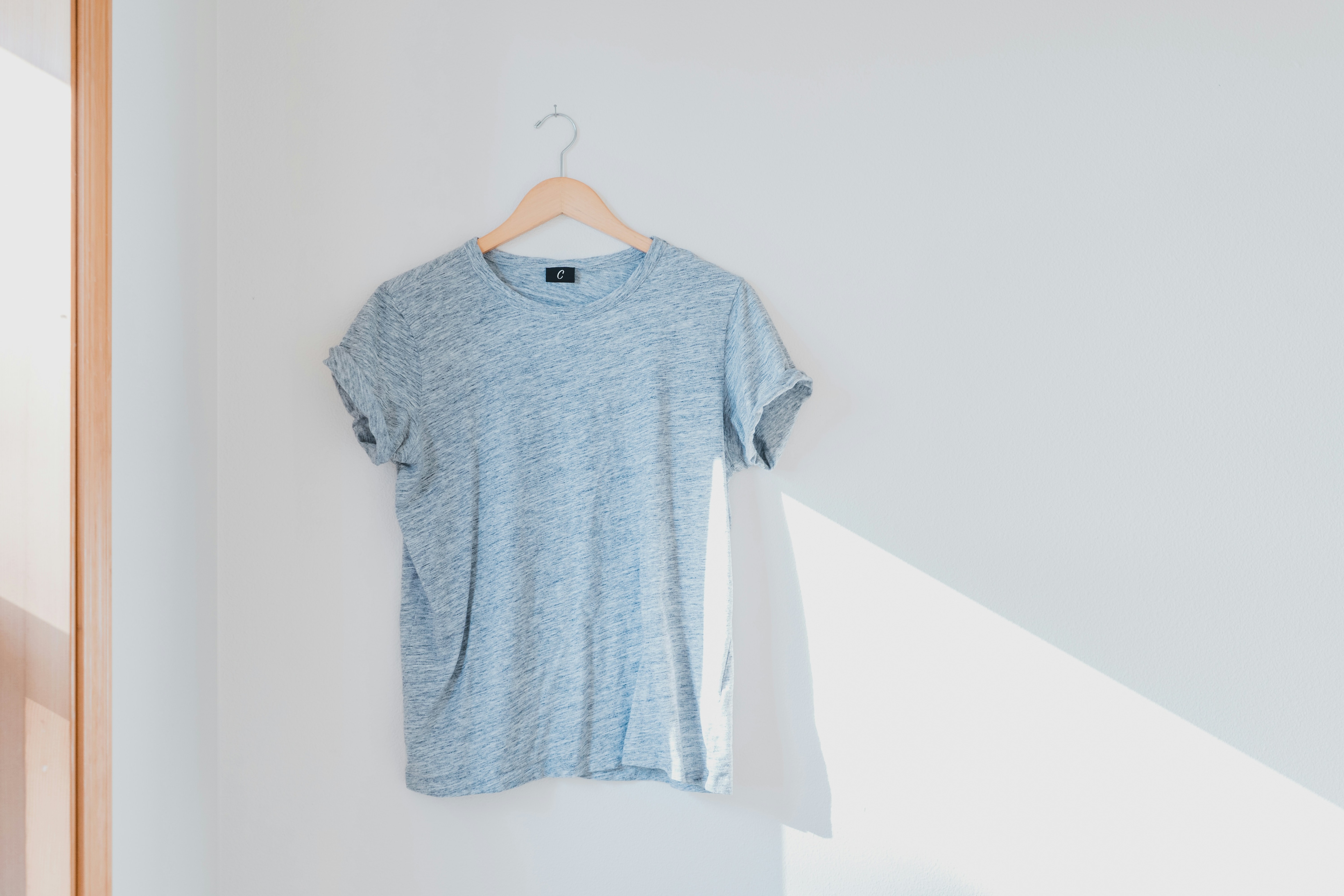 A light blue t-shirt hanging on a hanger against a white wall.