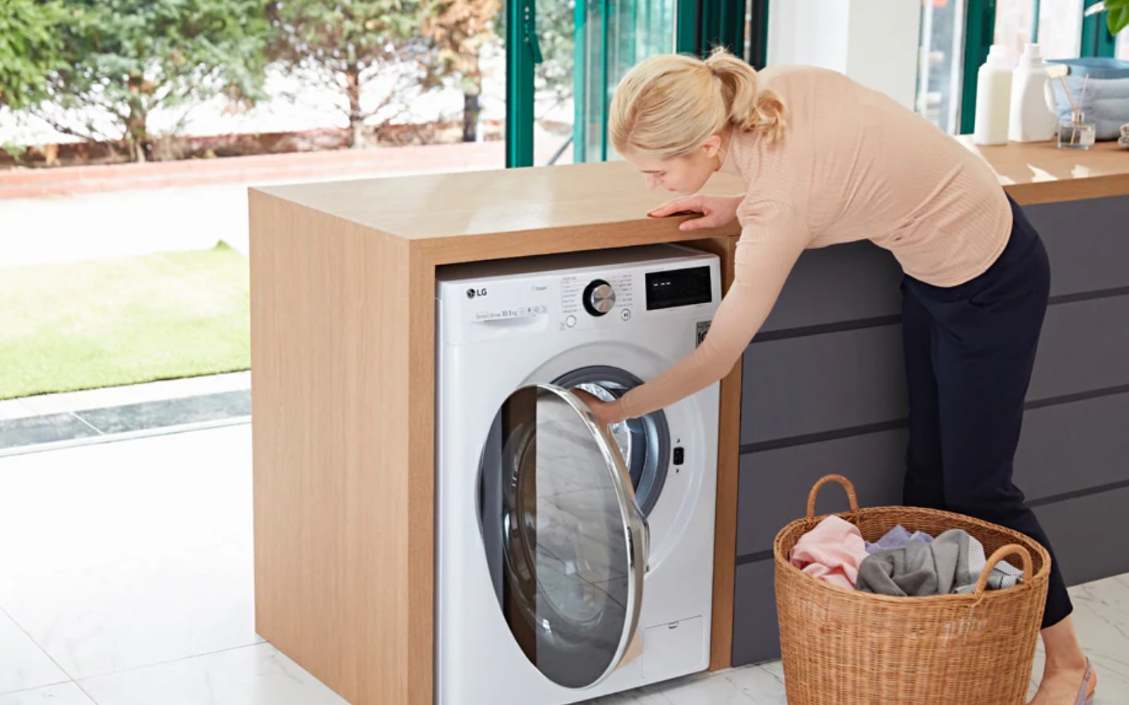 A woman loading laundry into an LG washing machine in a stylish kitchen, demonstrating ease of use and advanced fabric care options.