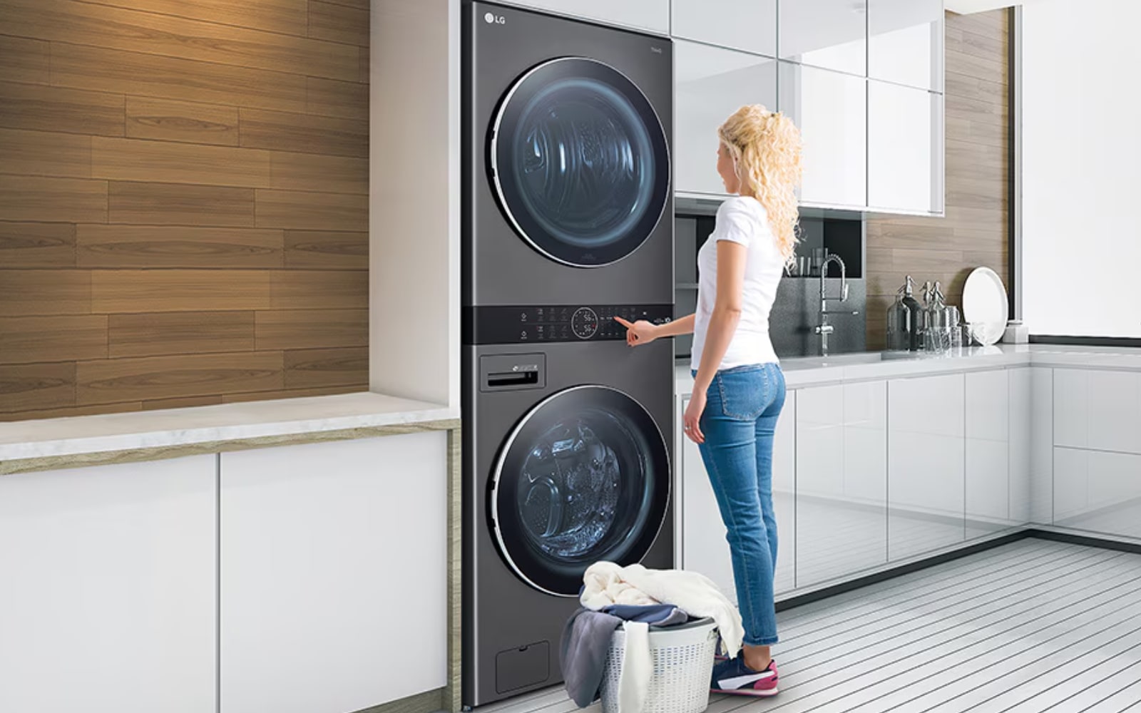 A woman using an LG stacked washer and dryer combo in a modern kitchen, showcasing space-saving design and efficient laundry care.