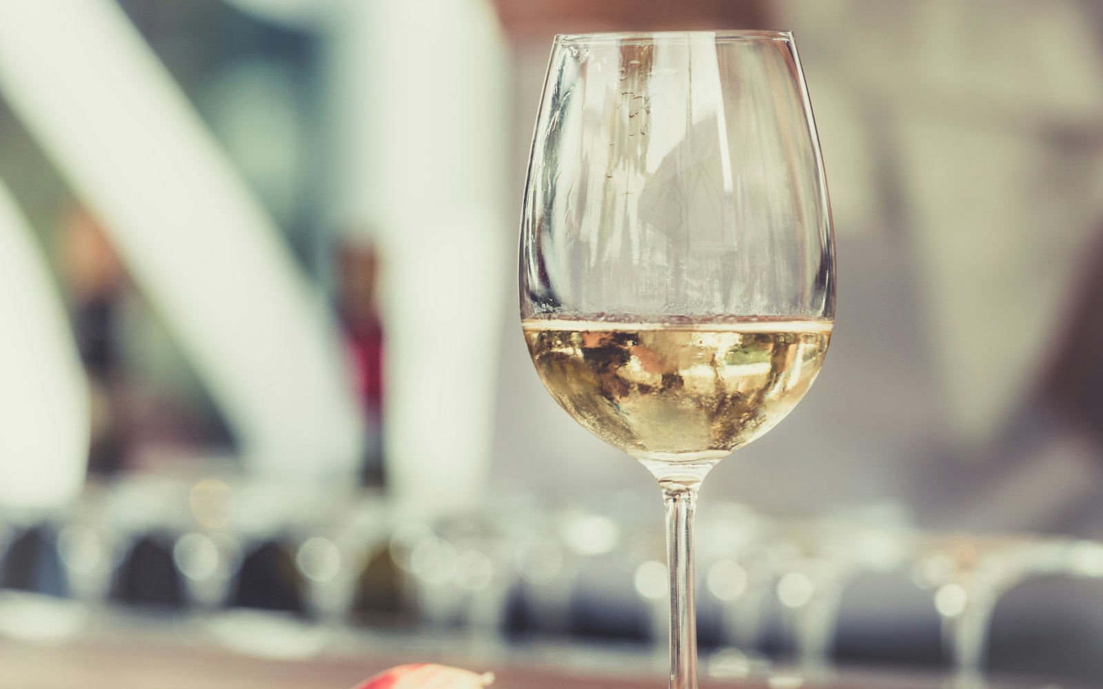 Close-up of a glass of white wine on a table with a blurred background, highlighting the elegant stemware and the sparkling wine inside.