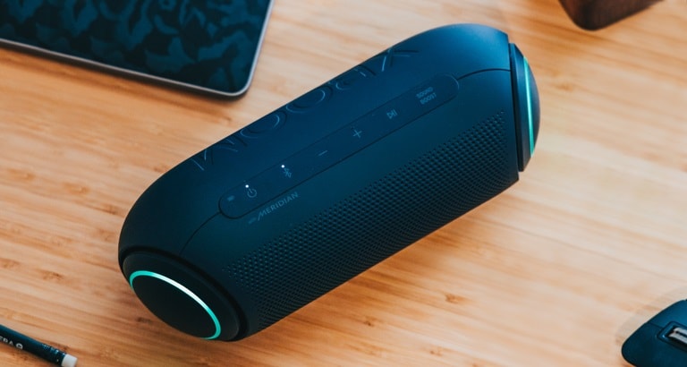 On a white backround, There is a close-up of LG XBOOM Go's Meridian logo with magenta lighting.
