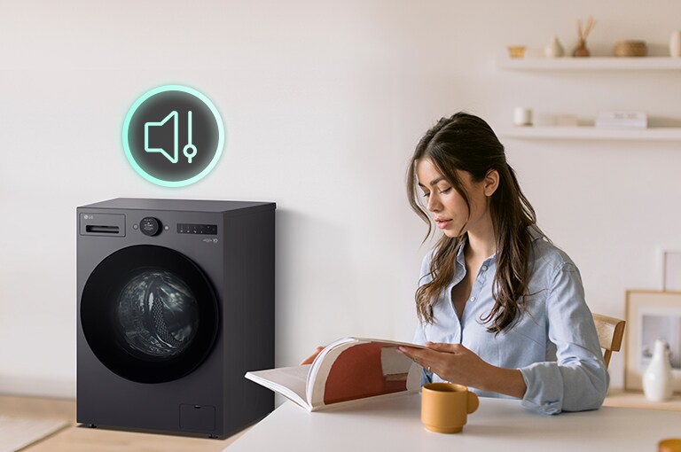The woman is sitting at a table reading a book and showing icons and washing machines that have less noise next to her