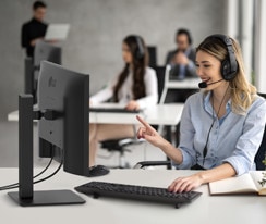 A woman is wearing a headset and working while looking at a monitor.