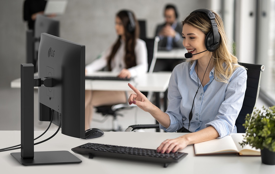 A woman is wearing a headset and working while looking at a monitor.