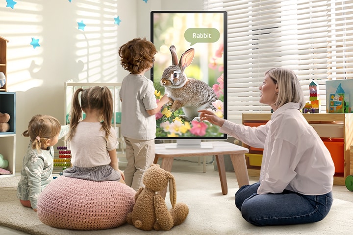 This picture shows a woman and three children playing using a LG Smart Monitor.