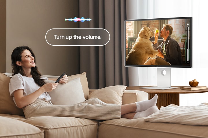 A woman is turning up the LG Smart Monitor’s volume using a Magic Remote.