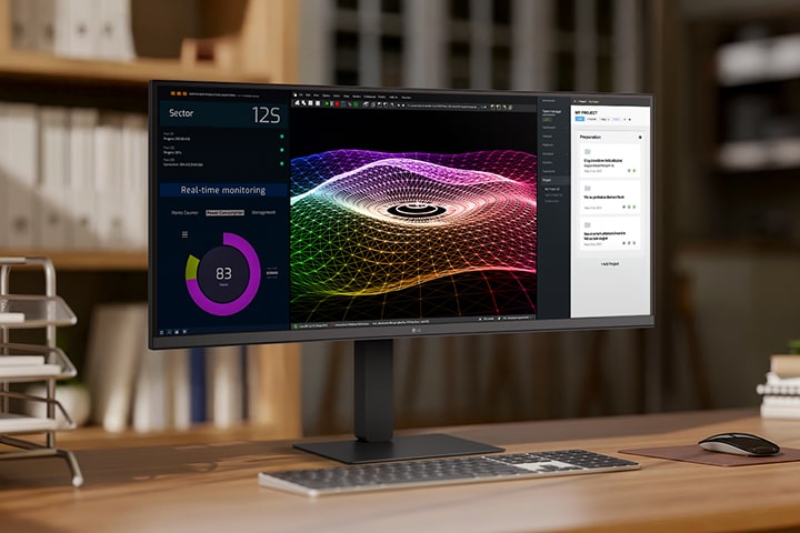 A modern home office setup featuring a large ultra-wide LG monitor displaying data dashboards and graphs, with a wireless keyboard and mouse on a wooden desk.