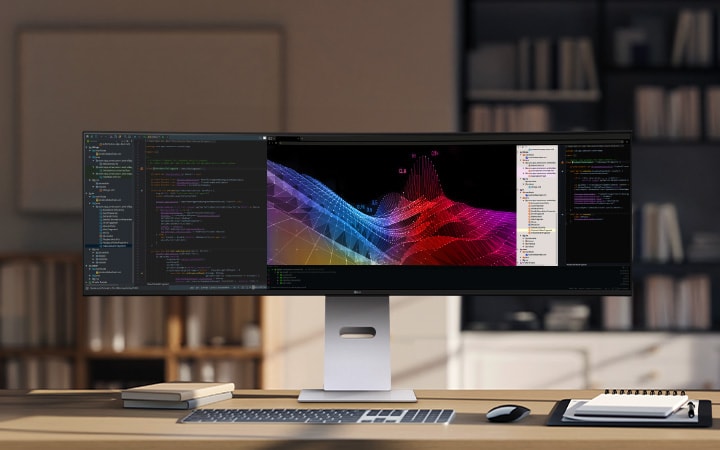 A modern home office setup featuring a large ultra-wide LG monitor displaying data dashboards and graphs, with a wireless keyboard and mouse on a wooden desk.