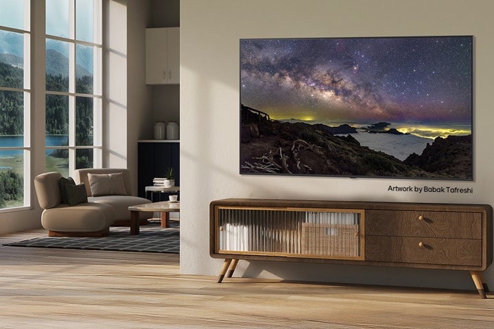 Interieur van een landelijk huis. Een grote, aan de muur gemonteerde LG TV toont een prachtig kunstwerk van een natuurlijk landschap op het scherm. De TV lijkt op een foto die aan de muur hangt. 