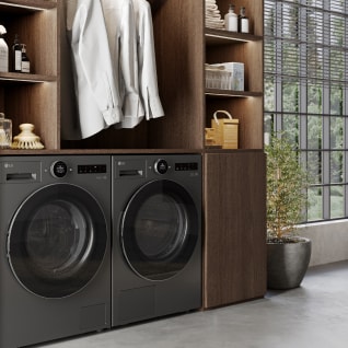 In de wasruimte staan een zwarte LG wasmachine en droger naast elkaar, naast een houten lade met wasmiddelen en overhemden erop.