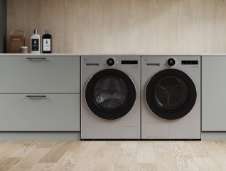 In de wasruimte staan een zilveren LG wasmachine en droger naast elkaar, met grijze laden ernaast.
