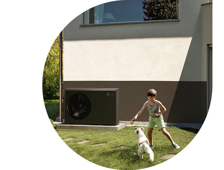 Een jongen speelt met een hond in de tuin van het huis en een nieuwe zwartgekleurde LG THERMA V is geïnstalleerd bij het voorste deel van de muur van het huis.