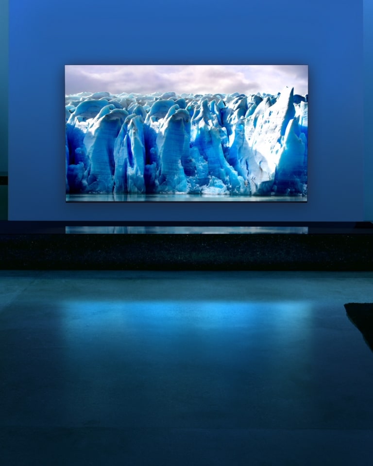 Een blauw neoncircuit beweegt rond op een blauw gletsjerbeeld. De camera zoomt uit en toont deze blauwe gletsjer op het tv-scherm. De tv is geplaatst in een brede woonkamer met blauwe achtergrond.