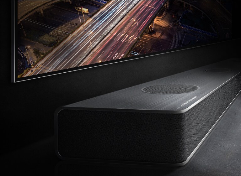 De rand van de soundbar is subtiel zichtbaar onder de tv met een nachtzicht op de weg.