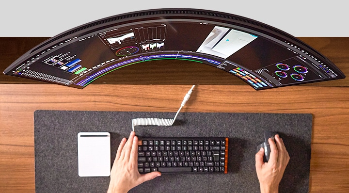 Persoon die aan een bureau werkt, handen gebruikend van muis en toetsenbord voor een brede monitor.