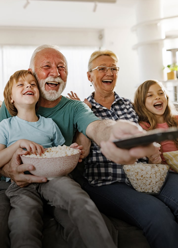 Een familie zit te lachen, terwijl de opa met de afstandsbediening naar buiten wijst.