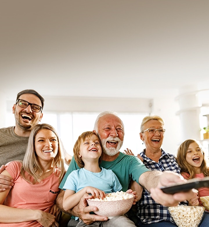 Een familie zit te lachen, terwijl de opa met de afstandsbediening naar buiten wijst.