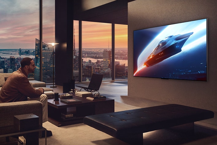 Elegante woonkamer in een penthouse-appartement. Prachtig stadsgezicht zichtbaar door het raam. Een man zit op de bank en kijkt naar een programma op de aan de muur bevestigde televisie.