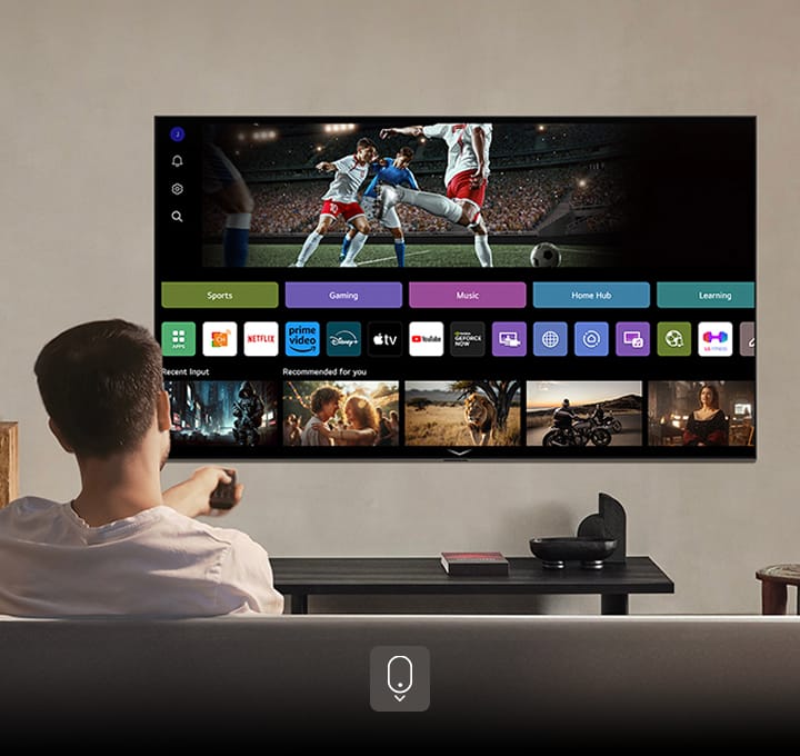 Een persoon op de bank die een afstandsbediening vasthoudt. Een LG AI TV aan de muur met LG webOS op het scherm.