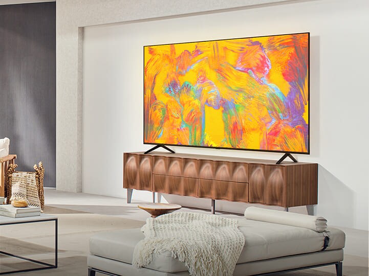 LG QNED TV boven een tv-lade in een gezellige leefruimte. LG QNED TV toont een abstracte achtergrond in oranje, geel, paars en roze.