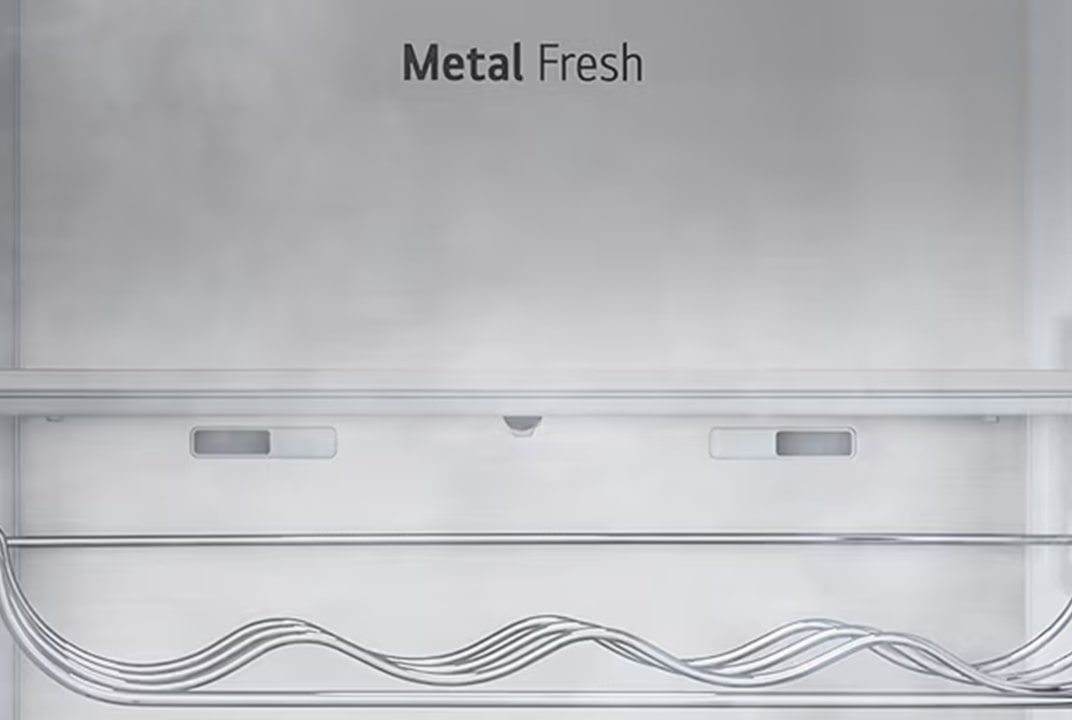 Close-up van het interieur van een koelkast met het label “Metal Fresh”, met een strakke metalen achterwand en een golvend metalen wijnrek onderaan.