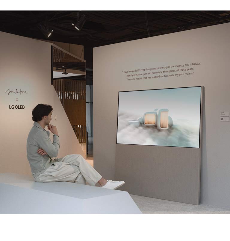 L’image montre une personne assise sur une chaise qui regarde un paysage onirique au milieu des nuages sur l’Easel. Sur un autre mur, un écran LG OLED montre une image d’arbres enneigés s’élevant vers le ciel.