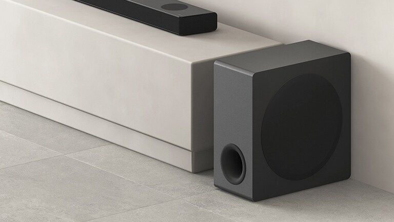 De subwoofer staat naast de beige plank in de woonkamer.