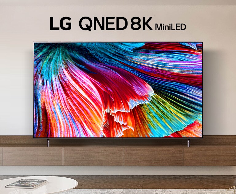 QNED MiniLED TV staat op een houten kast tegen een lichte muur in een licht modern interieur. Op het scherm is een close-up te zien van bloemblaadjes die uitwaaieren.