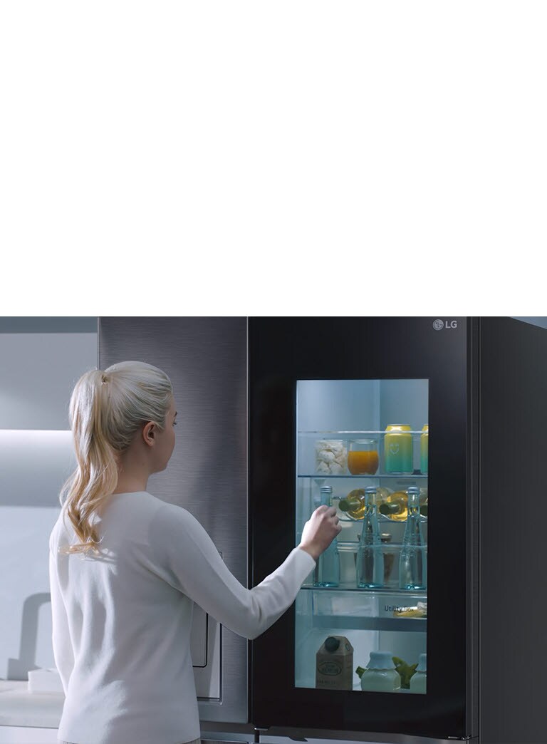 Een vrouw klopt op de InstaView koelkast en haalt een fles water eruit