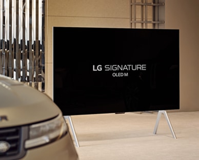 LG SIGNATURE OLED M4 op een standaard in het Range Rover House naast de Range Rover Sport SV, en een afspeelknop onder in beeld.