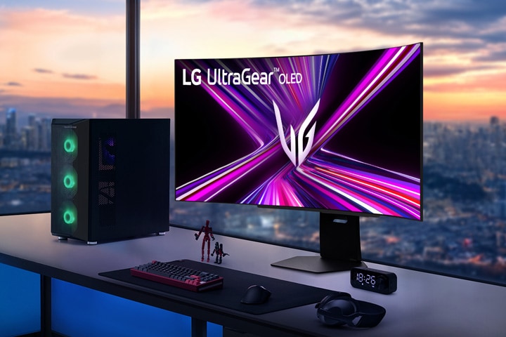 LG UltraGear OLED-monitor op een gamingbureau met een pc-opstelling, met uitzicht op een stadsgezicht bij zonsondergang.