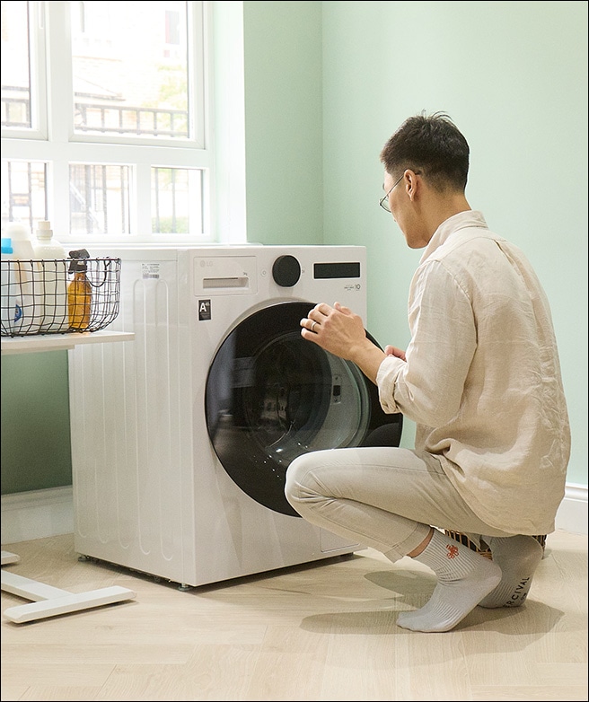 Homme chargeant le linge dans une machine à laver tout en réglant les paramètres.
