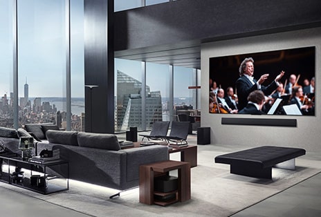 Sala de estar com uma LG True Wireless TV e uma LG Soundbar montada na parede. A Zero Connect Box mal pode ser vista sob uma mesa lateral ao lado do sofá, mostrando como pode ser facilmente colocada em qualquer lugar. Todo o layout da sala de estar é visualmente limpo e organizado.