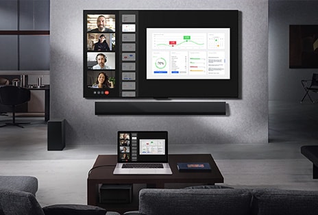 Sala de estar com vista do sofá, de frente para uma LG True Wireless TV montada na parede e uma LG Soundbar. Na mesa de centro há um laptop conectado à Zero Connect Box, que mal pode ser vista sob a mesa. A tela do laptop, que tem uma chamada de vídeo ao vivo, é espelhada sem fio na tela da TV. Todo o espaço é organizado e livre de fios.