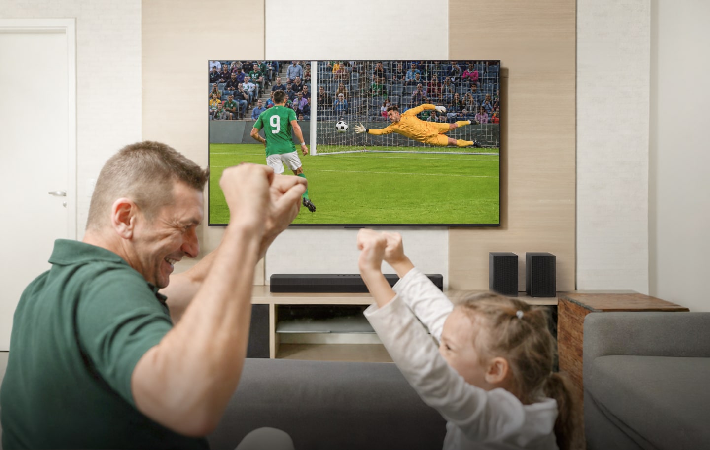 Gran televisor LG montado en la pared con una barra de sonido y un subwoofer, mostrando a un futbolista celebrando un gol.
