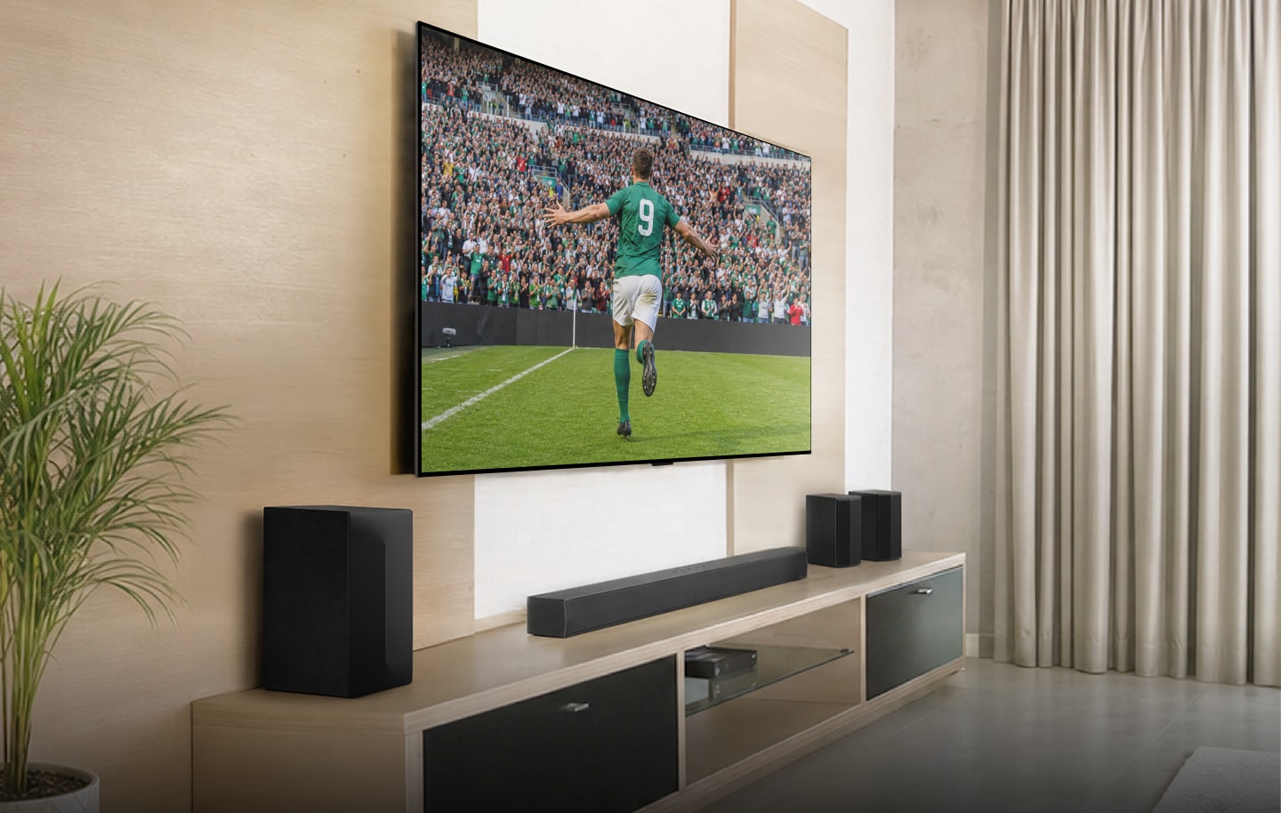 Grande TV LG montada na parede com soundbar e subwoofer, exibindo um jogador de futebol comemorando um gol.