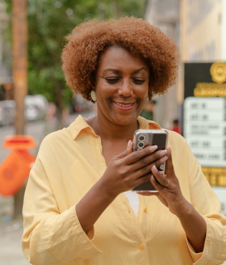 Sandra sorri enquanto olha o celular em uma rua da cidade.