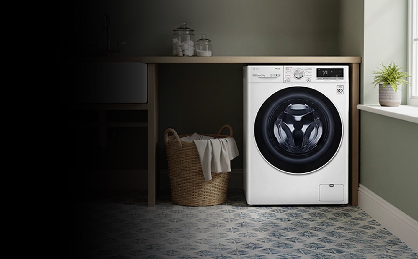 A black front-loading washing machine stands beside wood cabinets, with folded towels on a nearby rack.