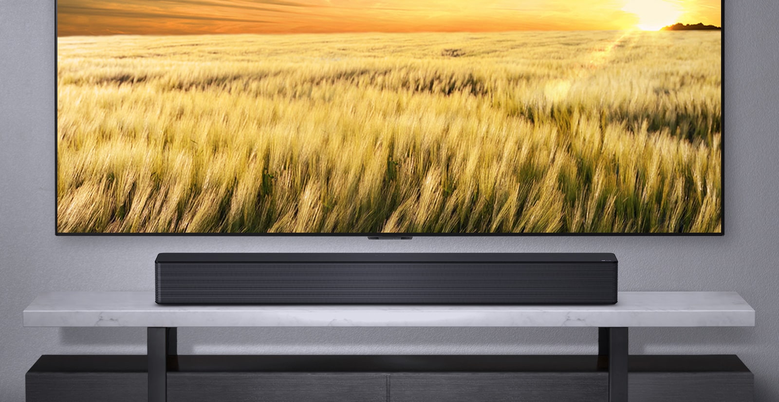 Uma TV é exibida em uma parede cinza e o LG Soundbar abaixo dela em uma prateleira cinza. Disco Blue-Ray abaixo da prateleira.
